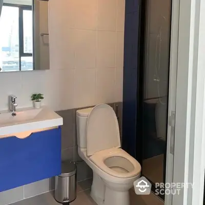 Compact modern bathroom with a sleek design, featuring a white toilet, blue vanity, and a glass shower enclosure.