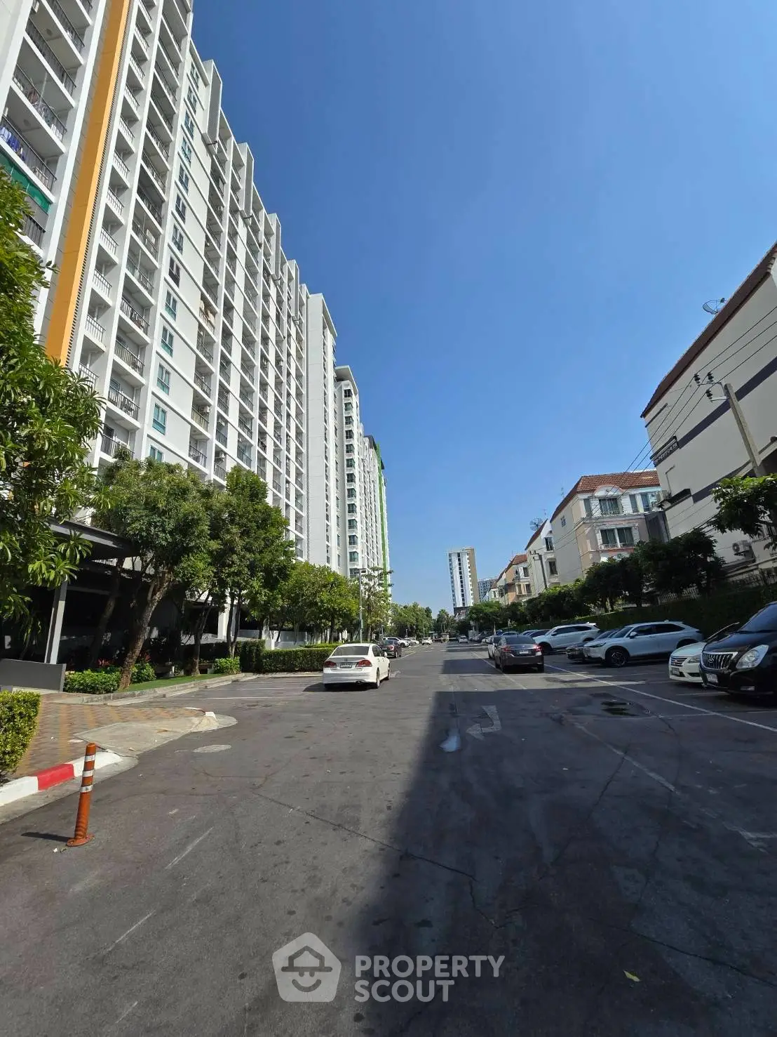 Modern high-rise residential building with street view and parked cars under clear blue sky.