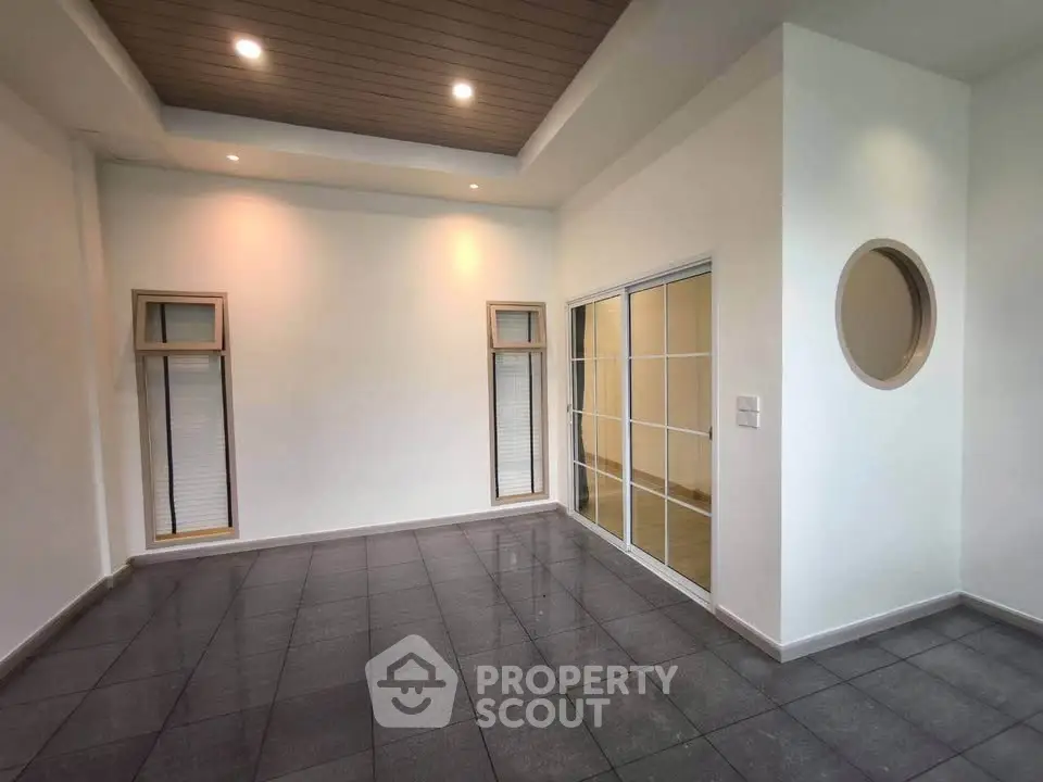 Spacious modern room with sleek tile flooring and stylish ceiling lights, featuring large windows and sliding glass doors.