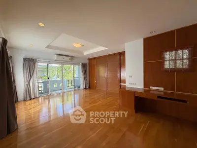 Spacious living room with wooden flooring and large windows offering natural light and garden view.