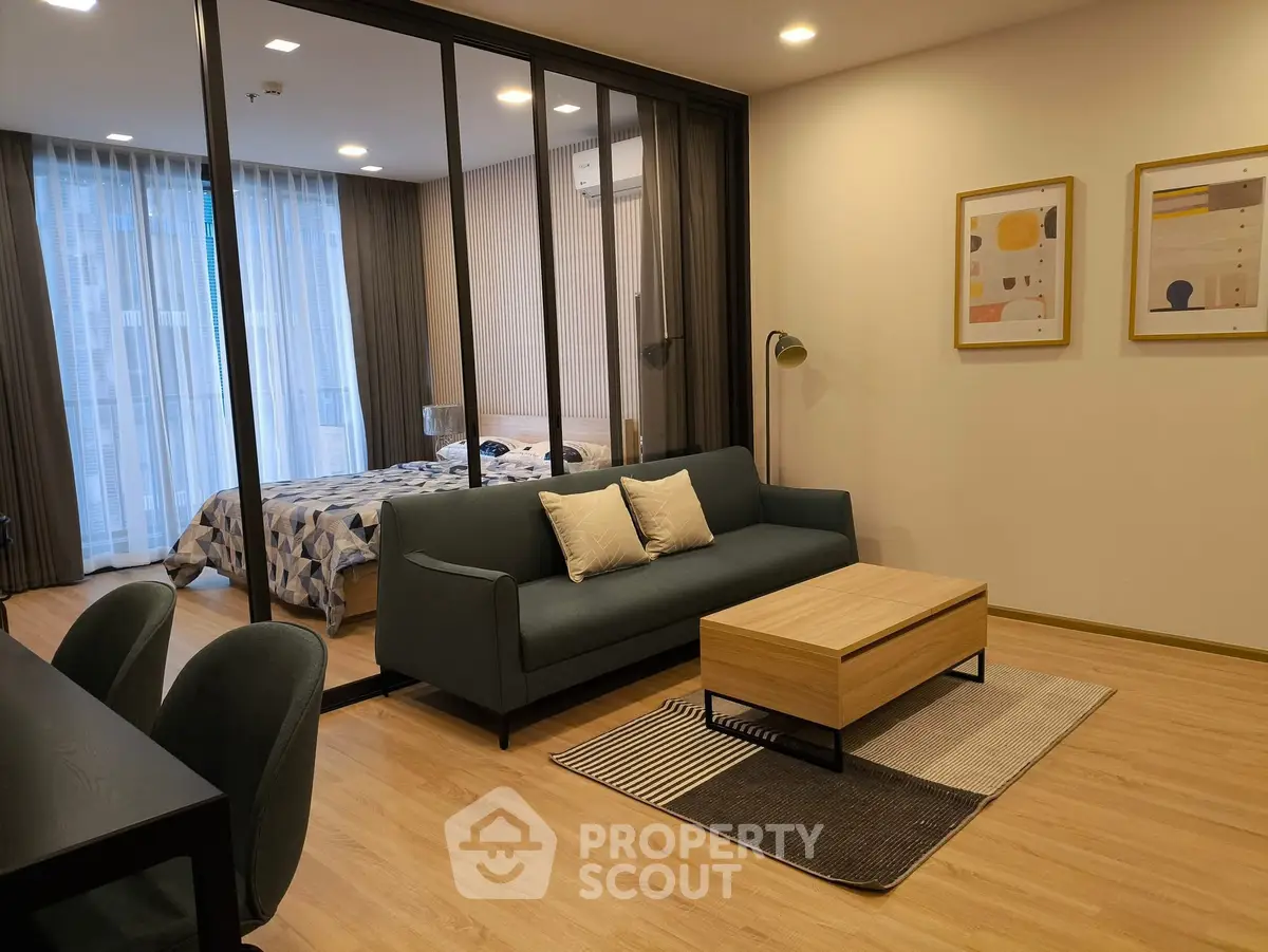 Modern living room with stylish decor and view into cozy bedroom, featuring elegant furniture and warm lighting.