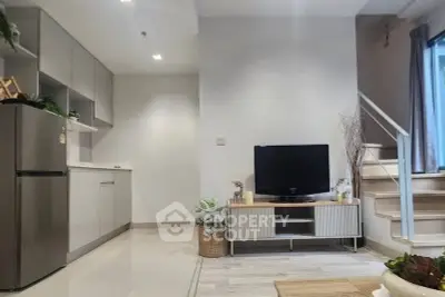 Modern open-plan living room with kitchen and staircase, featuring sleek design and natural light.