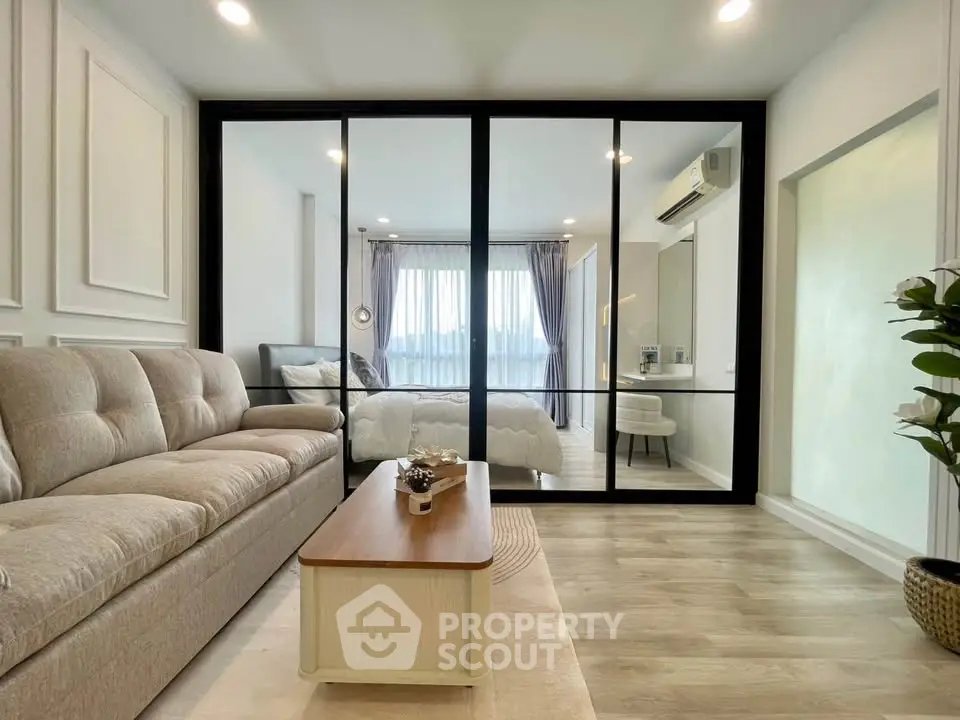 Modern living room with glass partition leading to a cozy bedroom