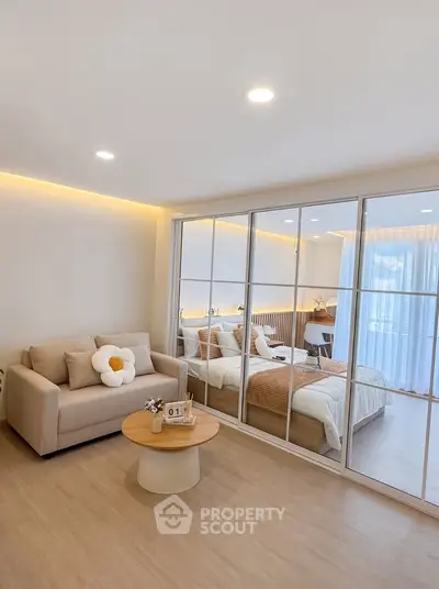 Modern bedroom with mirrored closet and cozy seating area, featuring elegant decor and natural light.
