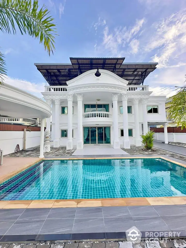 Luxurious mansion with grand entrance and private pool under clear blue sky.