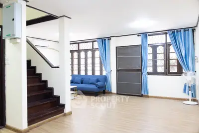 Spacious living room with wooden flooring and blue curtains, featuring a cozy sofa and staircase.