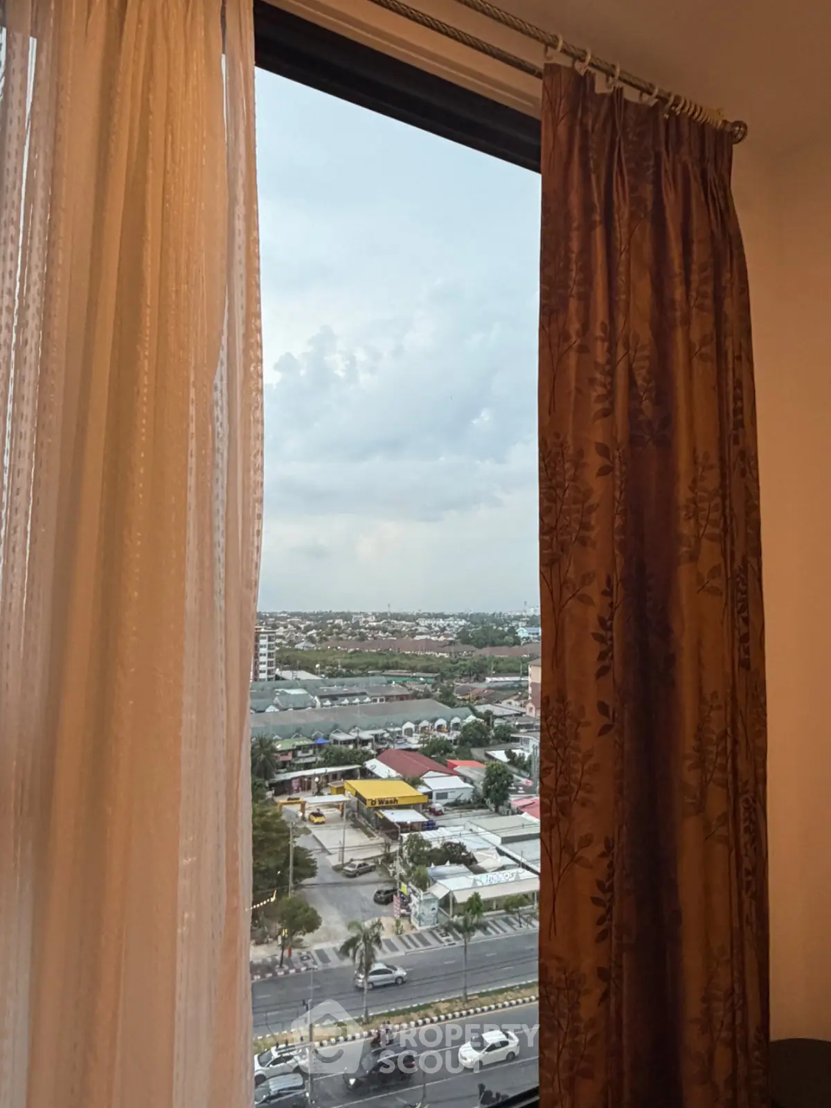 Stunning cityscape view from a high-rise apartment window with elegant curtains framing the scene.