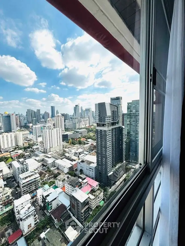 Stunning cityscape view from high-rise apartment window with blue sky and clouds.