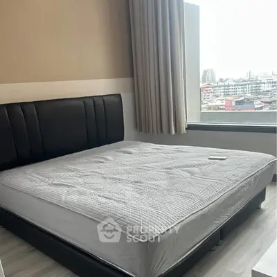 Modern bedroom with large window offering city view, featuring a stylish bed and neutral decor.