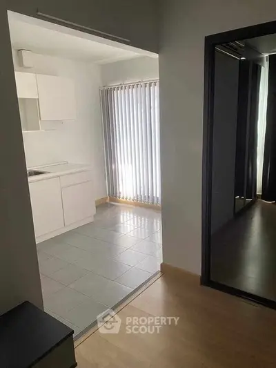 Modern minimalist kitchen with sleek white cabinets and natural light from vertical blinds.