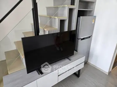 Modern interior with sleek staircase, TV, and stainless steel fridge in stylish living space.