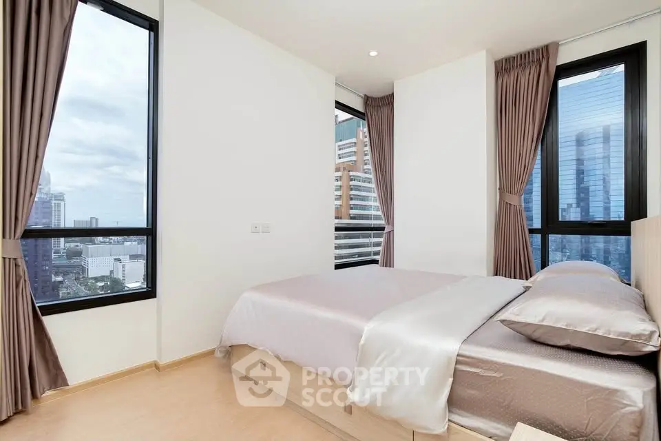 Modern bedroom with large windows offering stunning city views in a high-rise apartment.