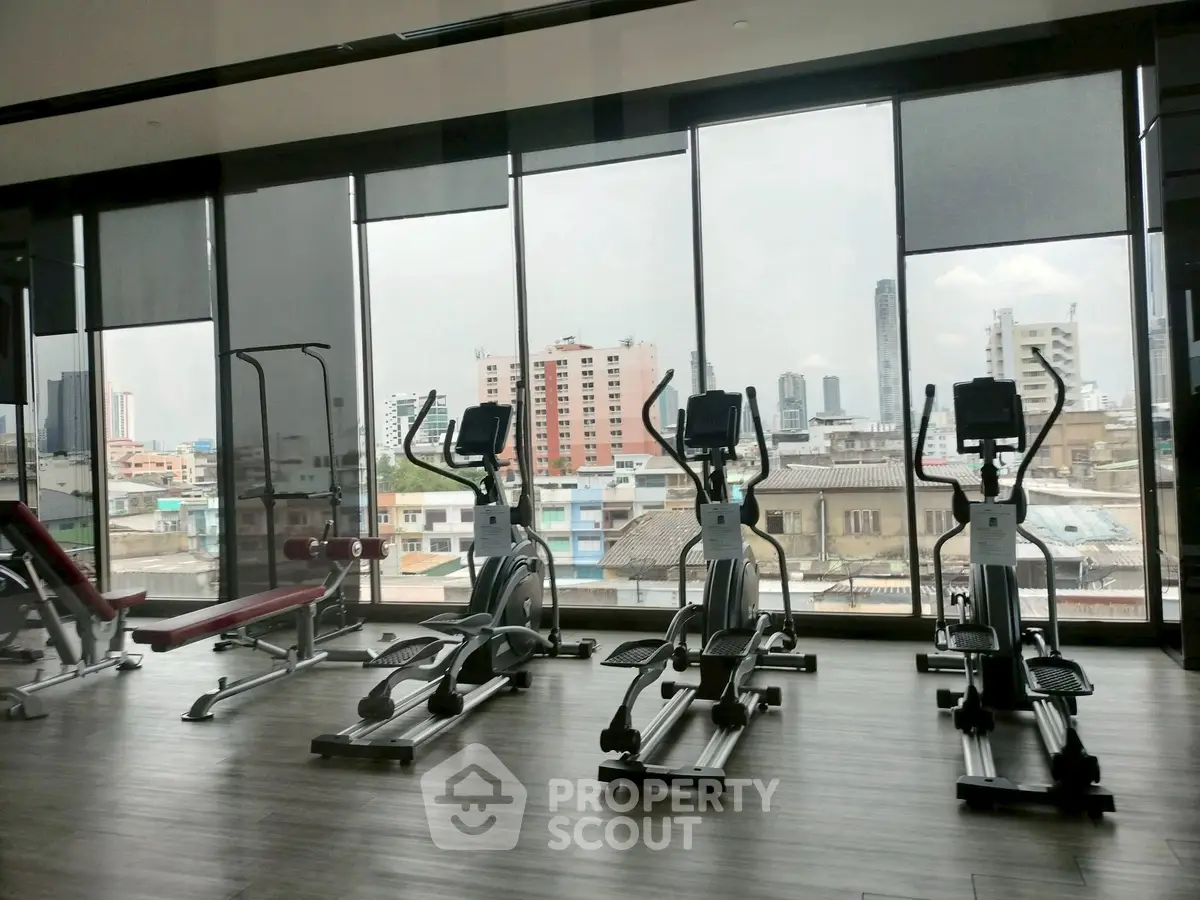 Modern gym with city view, featuring exercise equipment and large windows.
