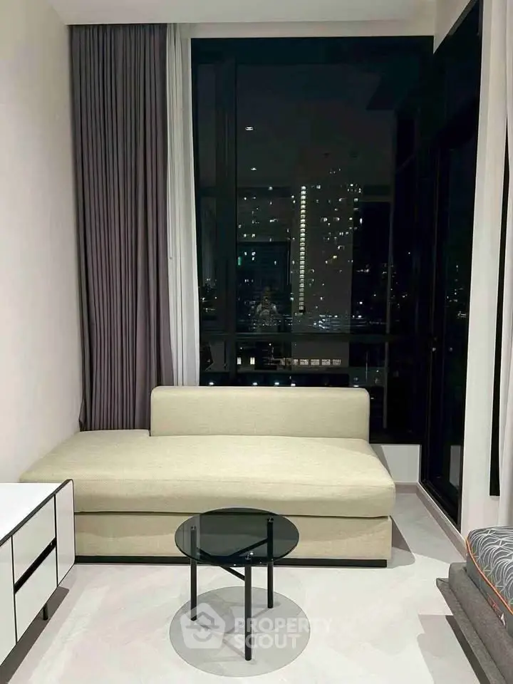Modern living room with city view, featuring a sleek sofa and glass coffee table.