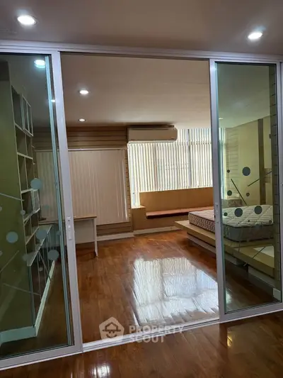 Spacious bedroom with wooden flooring and sliding glass doors in modern apartment.