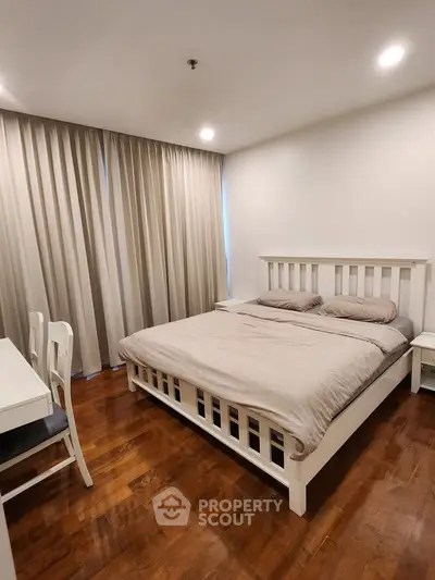 Cozy bedroom with wooden flooring and elegant curtains, featuring a comfortable bed and stylish furniture.