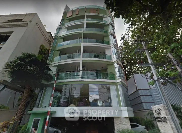 Modern multi-story building with balconies and lush greenery in urban setting.