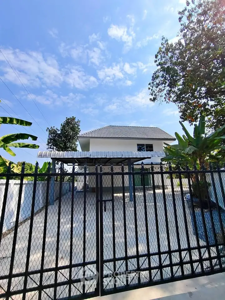 Charming two-story house with gated driveway and lush greenery under a clear blue sky.