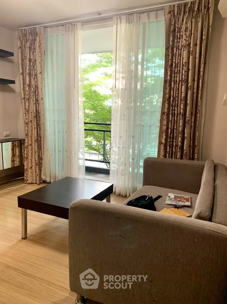 Cozy living room with modern sofa and coffee table, featuring a view of lush greenery through large windows.