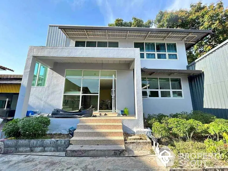 Modern two-story house with large windows and garden in sunny setting