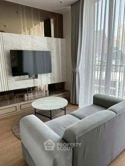 Modern living room with sleek design, featuring a wall-mounted TV and large windows offering city views.