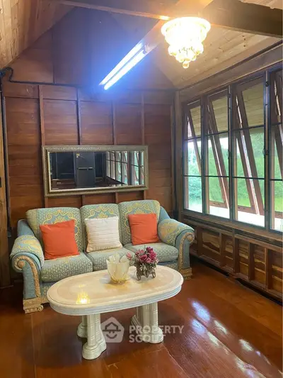 Charming rustic living room with wooden walls, elegant chandelier, and cozy seating area.