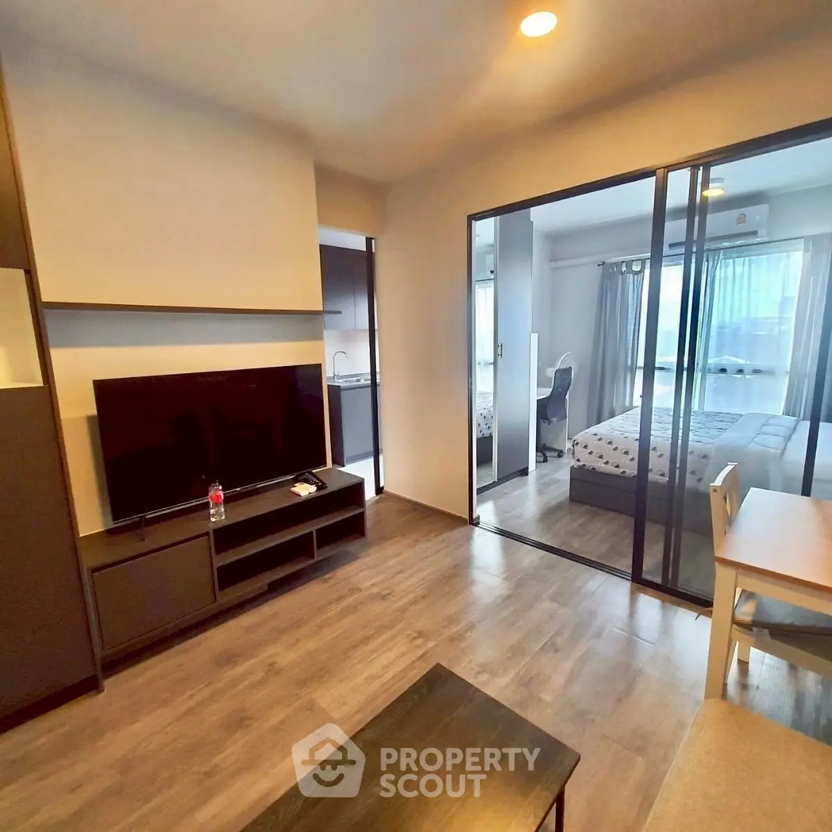 Modern open-plan living room with glass partition to bedroom, featuring sleek furniture and natural light.