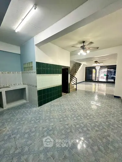Spacious open-plan living area with tiled floors and ceiling fans, featuring a staircase and ample natural light.