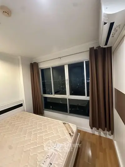 Modern bedroom with city view, featuring large window and air conditioning unit.