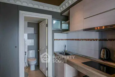 Compact kitchen with modern appliances and adjacent bathroom in a stylish apartment.