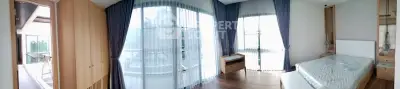 Spacious bedroom with large windows and balcony access, featuring modern wooden furnishings and elegant curtains.