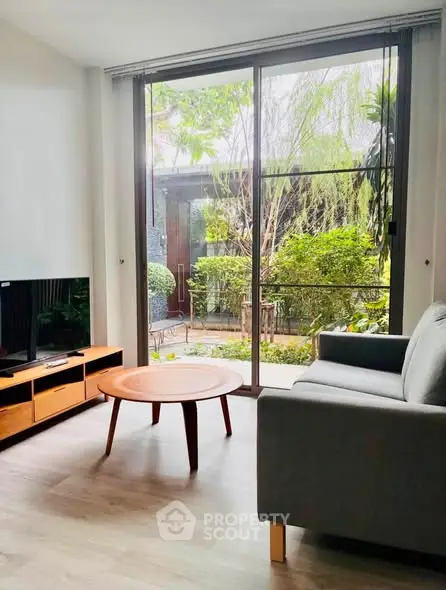 Modern living room with large window overlooking lush garden, featuring sleek furniture and natural light.
