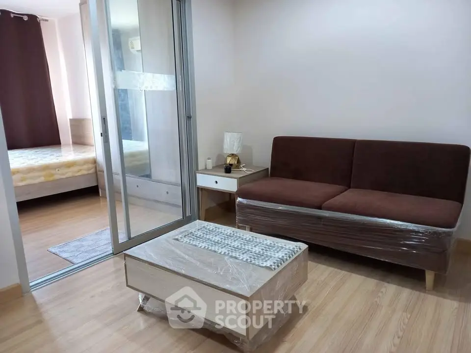Modern living room with sliding glass door leading to a cozy bedroom, featuring stylish furniture and wooden flooring.