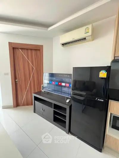 Modern living room with sleek black fridge and wall-mounted TV, featuring stylish wooden door and air conditioning.