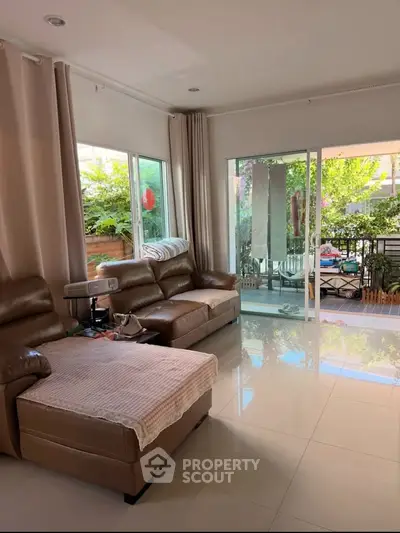 Spacious living room with leather sofas and large windows opening to a lush garden view.