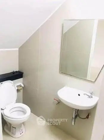 Compact bathroom with sloped ceiling, featuring a toilet, sink, and mirror.