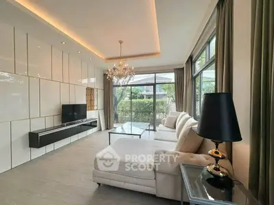 Luxurious living room with elegant chandelier and large windows offering garden views.