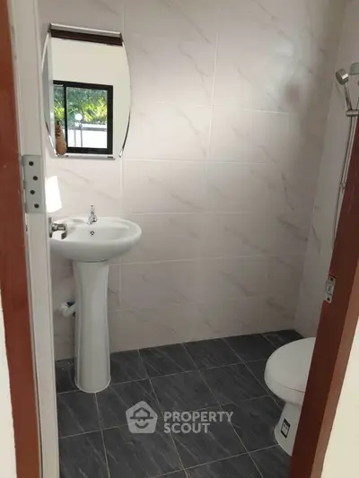 Modern bathroom with pedestal sink and tiled walls, featuring a sleek design.