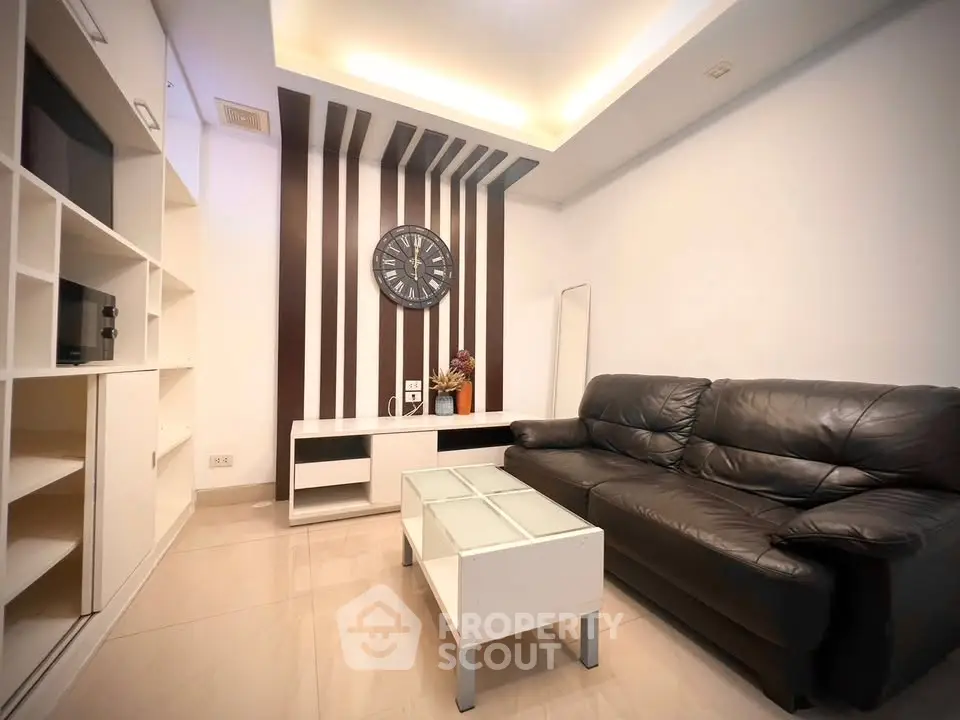 Modern living room with sleek black leather sofa and stylish wall clock, perfect for urban living.