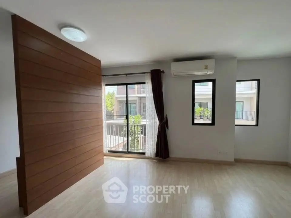 Spacious living room with wooden accent wall and balcony view in modern apartment.