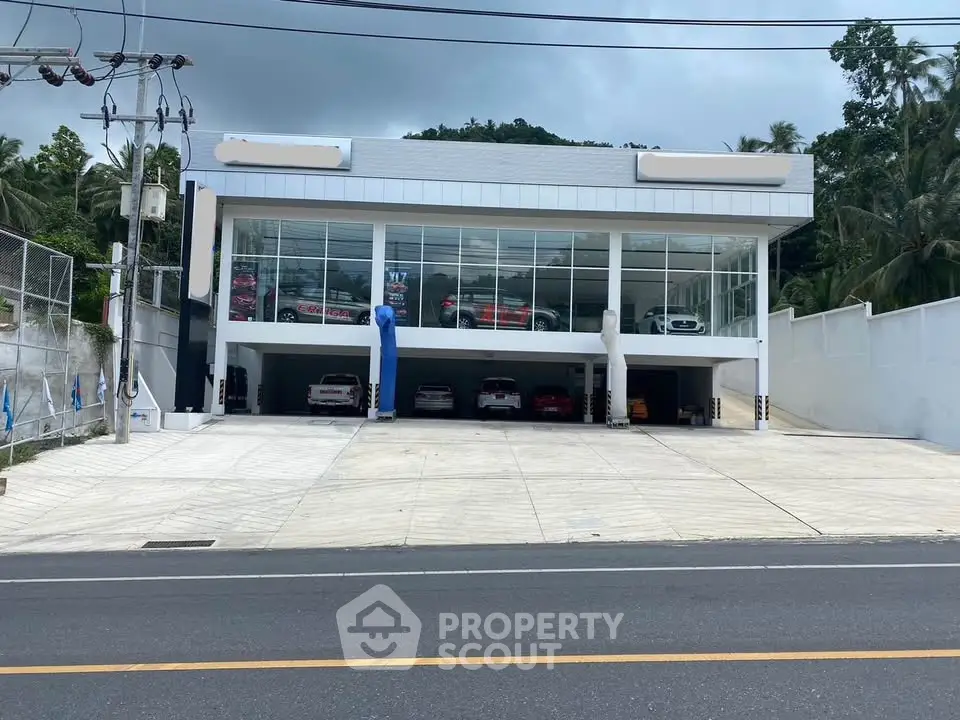 Modern commercial building with large glass facade and spacious parking area on a main road.