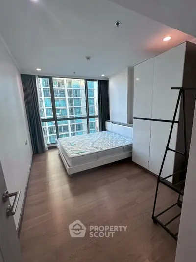 Modern bedroom with large window and city view, featuring sleek furniture and wooden flooring.