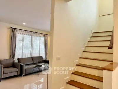 Modern living room with staircase and natural light, featuring stylish gray sofas and elegant decor.