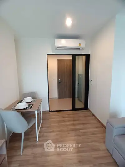 Modern apartment interior with wooden flooring, dining area, and sliding glass door.