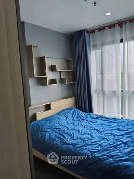 Cozy bedroom with modern shelving and blue bedding, natural light through large window.