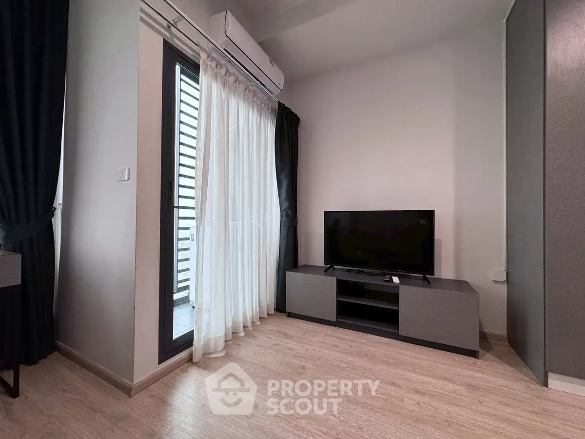 Modern living room with sleek TV setup and balcony access, featuring elegant curtains and air conditioning.