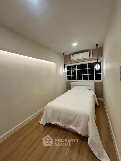 Cozy minimalist bedroom with wooden flooring and modern lighting.