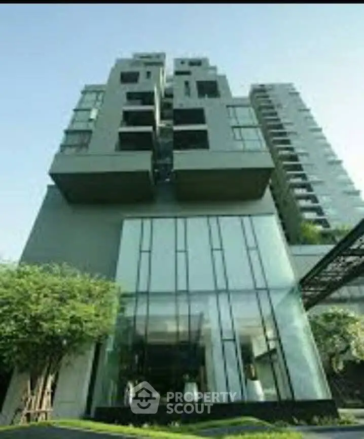 Modern high-rise building with sleek glass facade and lush greenery.