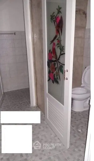 Charming bathroom with unique decorative door and tiled flooring.