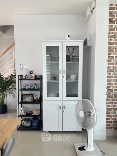Modern interior with white cabinet, fan, and decorative shelves in a stylish living space.